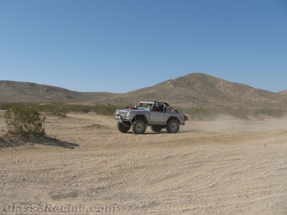 Silver vintage Ford Bronco-style off-road truck racing in the desert