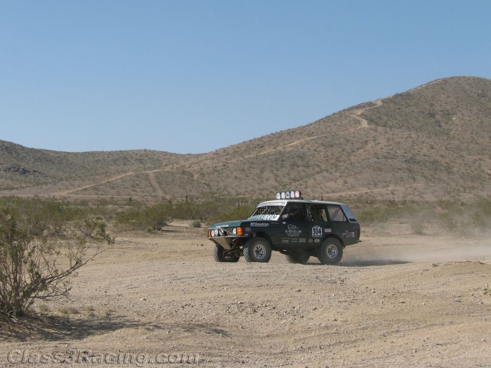 Teal and white early Ford Bronco-style race truck on a desert course