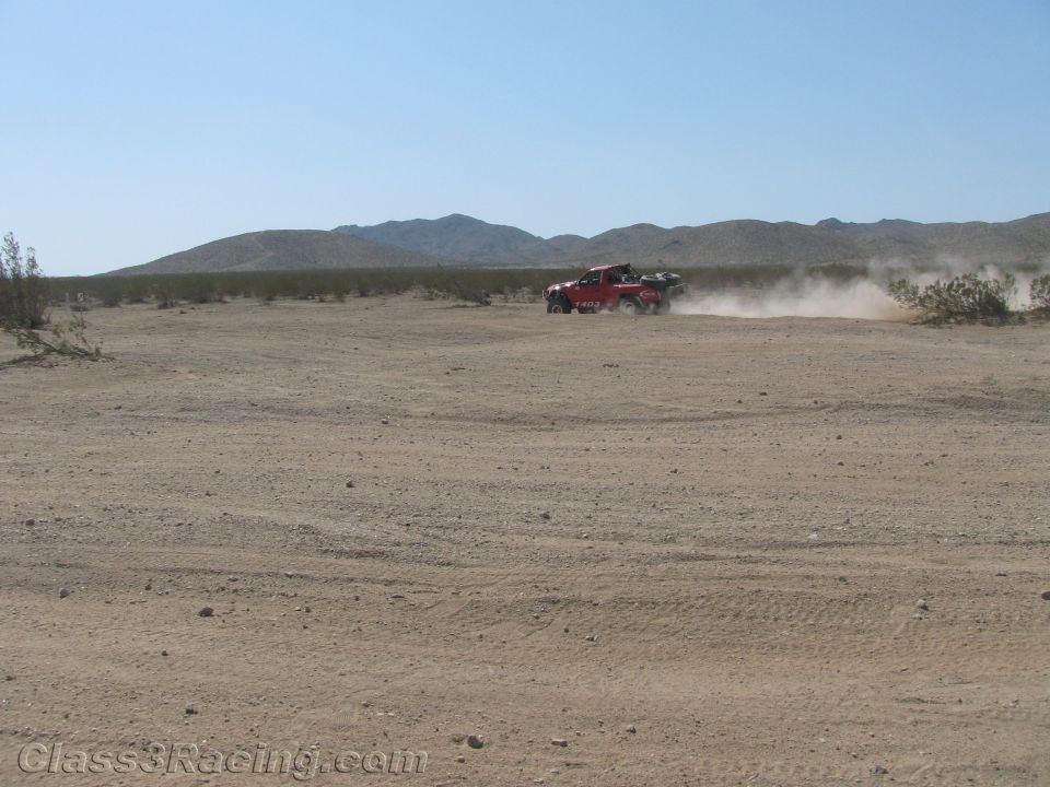 Red off-road truck racing in the distance across desert terrain