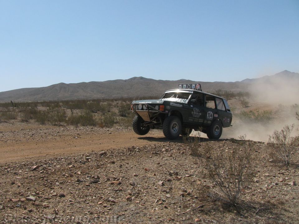 Black SUV-bodied off-road race truck jumping on a desert trail