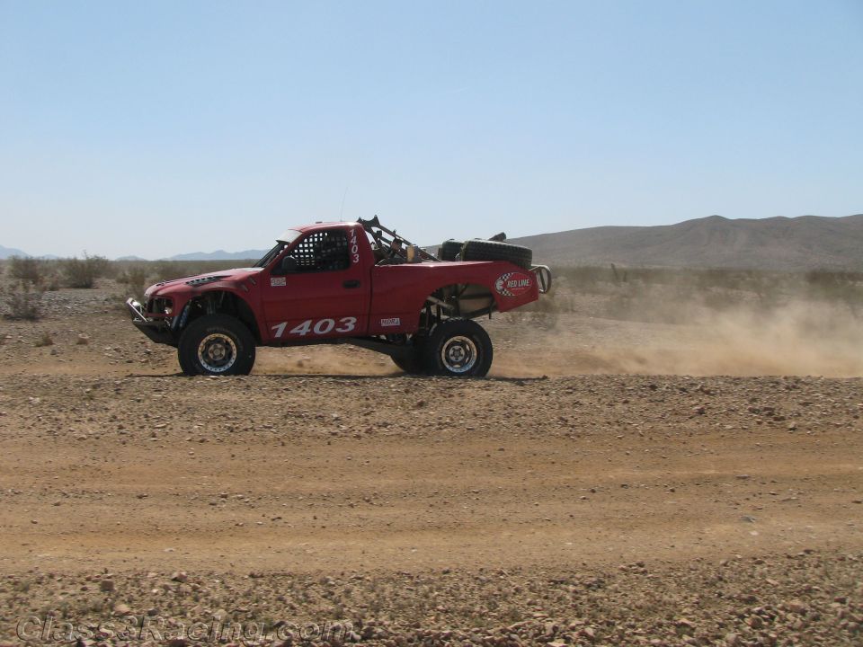 Red off-road race truck number 1403 speeding on a desert road