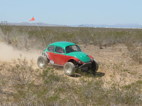 1990 Ford Bronco - green-topped, red-bodied Baja Volkswagen Beetle with an orange course flag drives through low desert brush.