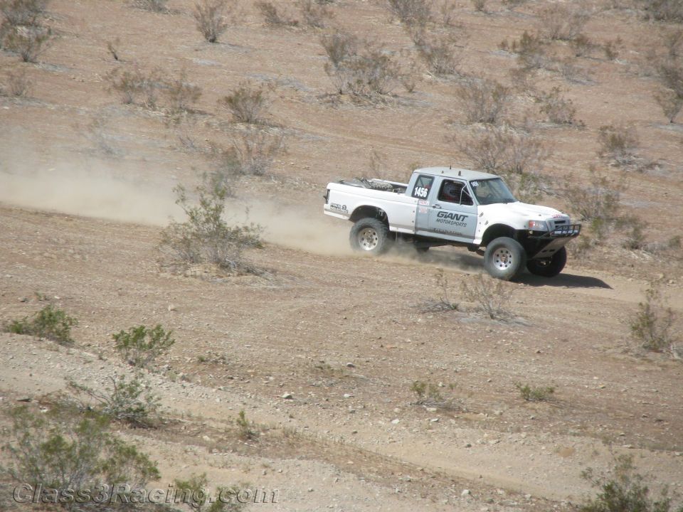 White off-road race truck speeding along a sloped desert trail