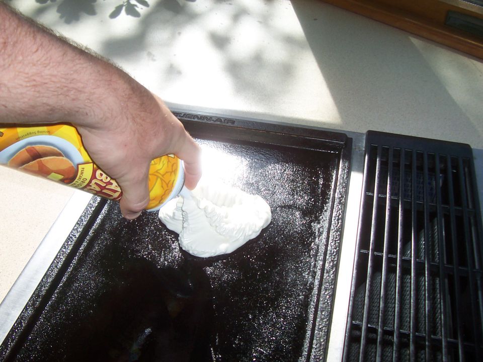 Hand pouring pancake batter onto a griddle next to a grill grate