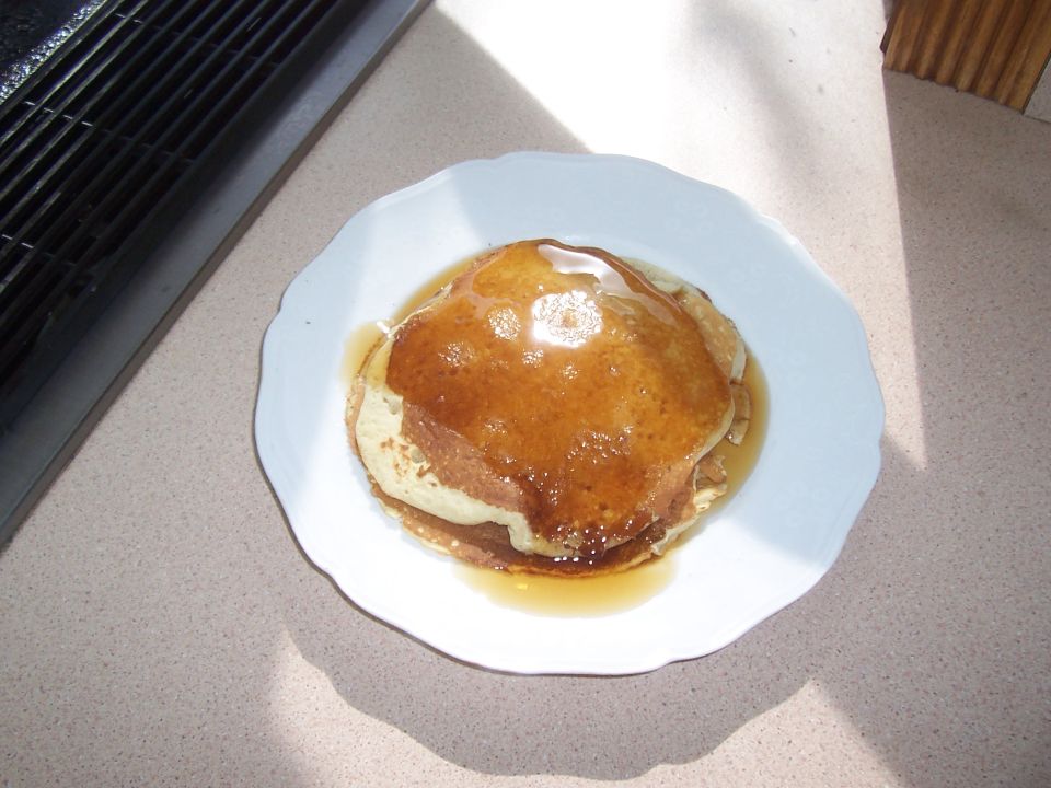 Plate of pancakes with syrup and butter on a countertop next to a black grill