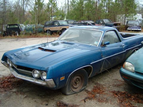 1979 Ford Ranchero - This blue pickup truck, likely from the early 1970s, sits with a flat tire in a junkyard setting.