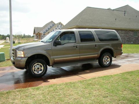 1995 Ford Bronco - A Ford Excursion SUV is parked on a wet driveway in front of unfinished houses.