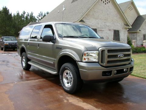 1995 Ford Bronco - A gray Ford Excursion is shown parked on a wet driveway in front of a house, with another vehicle visible in the background.