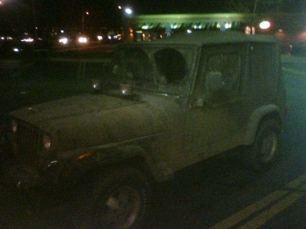 Mud-covered hardtop SUV with round headlights parked at night, front three-quarter view
