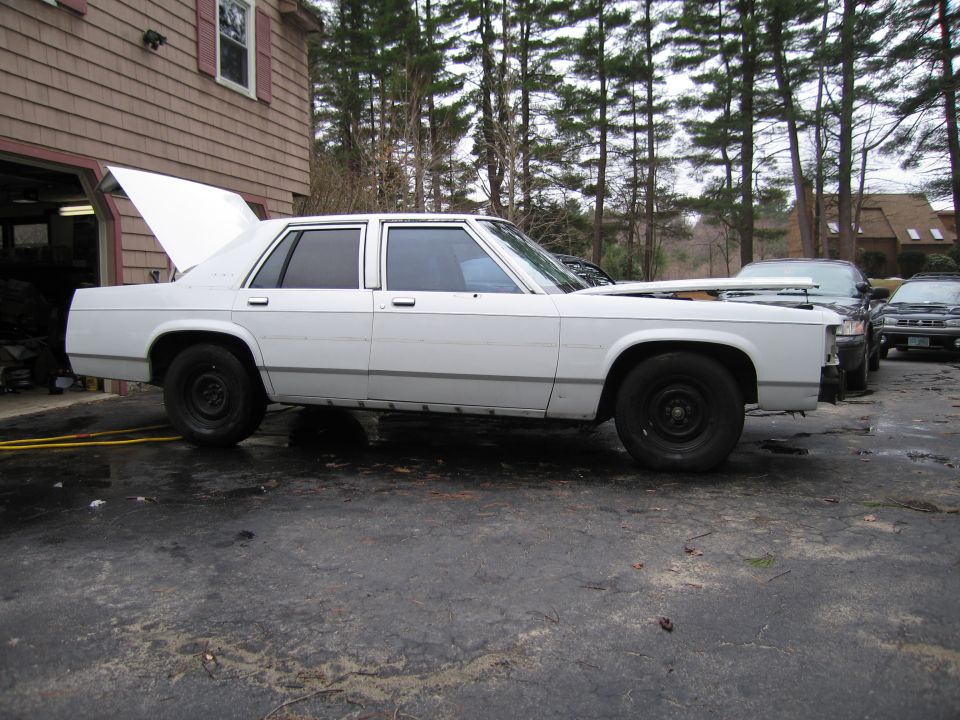 White sedan with hood open, parked in driveway next to other cars