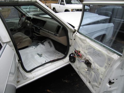 1991 Ford LTD Crown Victoria - The interior of a white 1991 Ford Crown Victoria LTD is shown with the driver's side door removed, revealing exposed wiring and interior co…