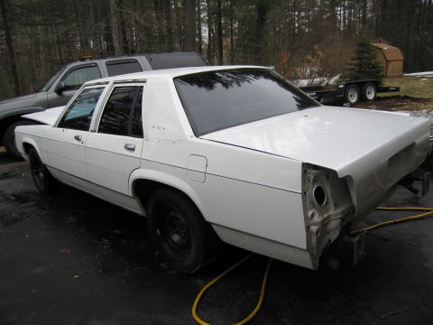 1991 Ford LTD Crown Victoria - This white sedan is missing its rear bumper and taillights, suggesting it is undergoing repairs or modifications.