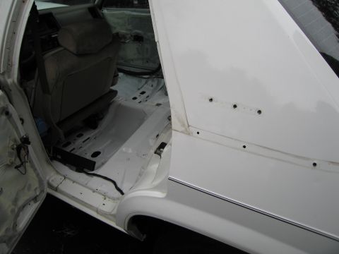 1991 Ford LTD Crown Victoria - Interior of a white sedan shows stripped floor and removed door panels, with a partial view of the exterior side exterior.