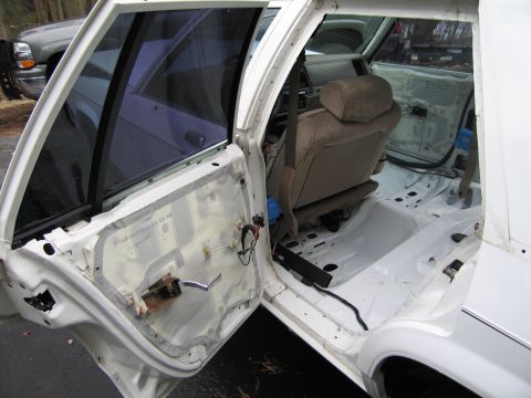 1991 Ford LTD Crown Victoria - The interior of a white car is shown with the driver's side door open, revealing a dismantled door panel and a stripped floor.