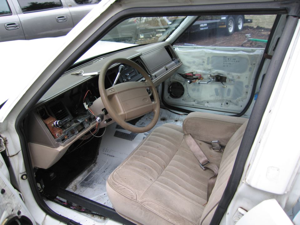 Interior of a car with tan seats and door panels removed, showing exposed wiring and a beige dashboard