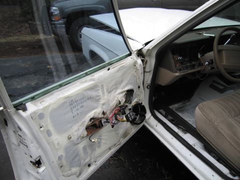 1991 Ford LTD Crown Victoria - Interior view of a white car with its driver's side door panel removed, revealing internal components and wiring.