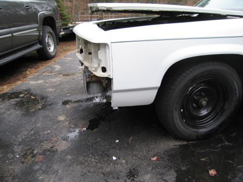 1991 Ford LTD Crown Victoria - Front view of a white car with its hood open and missing front-end components, parked next to another vehicle.