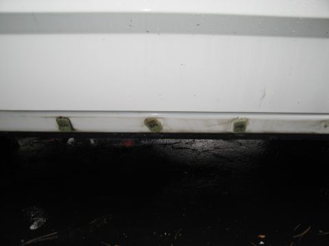 1991 Ford LTD Crown Victoria - The lower edge of a white car door shows several green clips securing trim, with a dark, wet surface below.