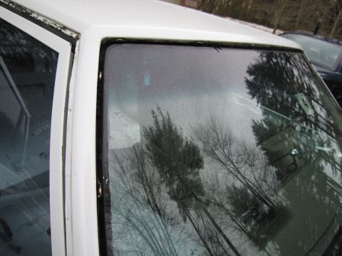 1991 Ford LTD Crown Victoria - Close-up view of a white car's windshield and door frame, with reflections of trees and another vehicle visible.
