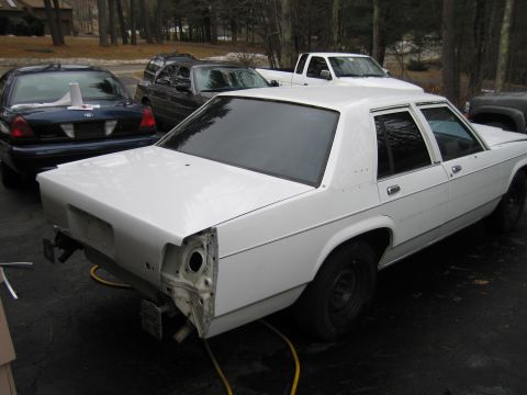 1991 Ford LTD Crown Victoria - A white sedan is parked outside with its rear bumper removed, indicating it is undergoing repairs or modifications.