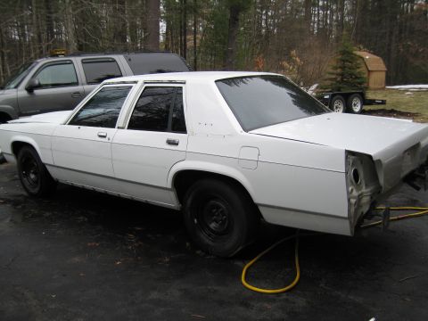 1991 Ford LTD Crown Victoria - A white sedan with black wheels is viewed from the rear, showing its unfinished bodywork.