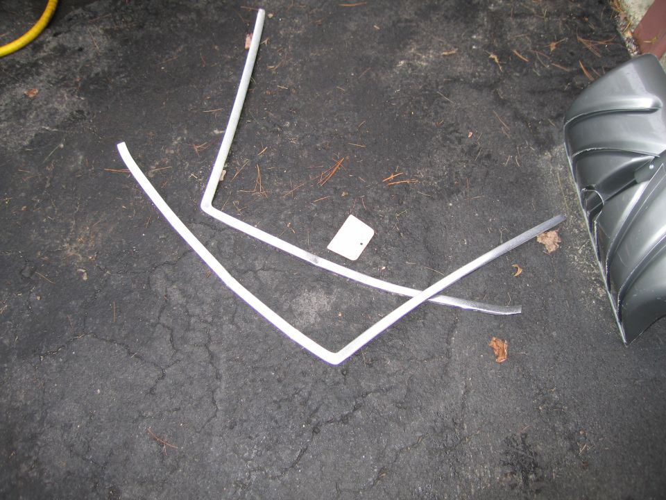 Chrome trim pieces and a gray car fender lying on asphalt