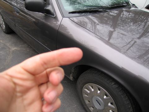 1991 Ford LTD Crown Victoria - A car's fender and wheel are visible, with a finger obscuring part of the view.