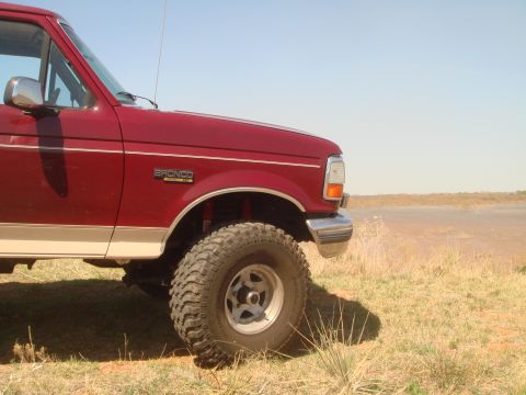 1992 Ford Bronco - Close-up of a red 1992 Ford Bronco's front fender, tire, and chrome bumper.