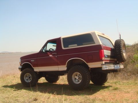 1992 Ford Bronco - This lifted Ford Bronco is parked on a grassy area overlooking a body of water under a clear blue sky.