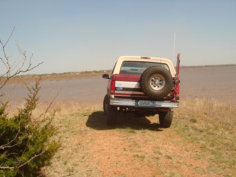 1992 Ford Bronco - A 1992 Ford Bronco is parked on a grassy bank overlooking a body of water under a clear blue sky.