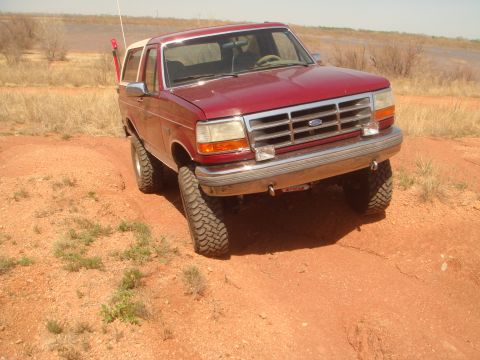 1992 Ford Bronco - A red 1992 Ford Bronco is shown driving on a dusty, off-road trail.