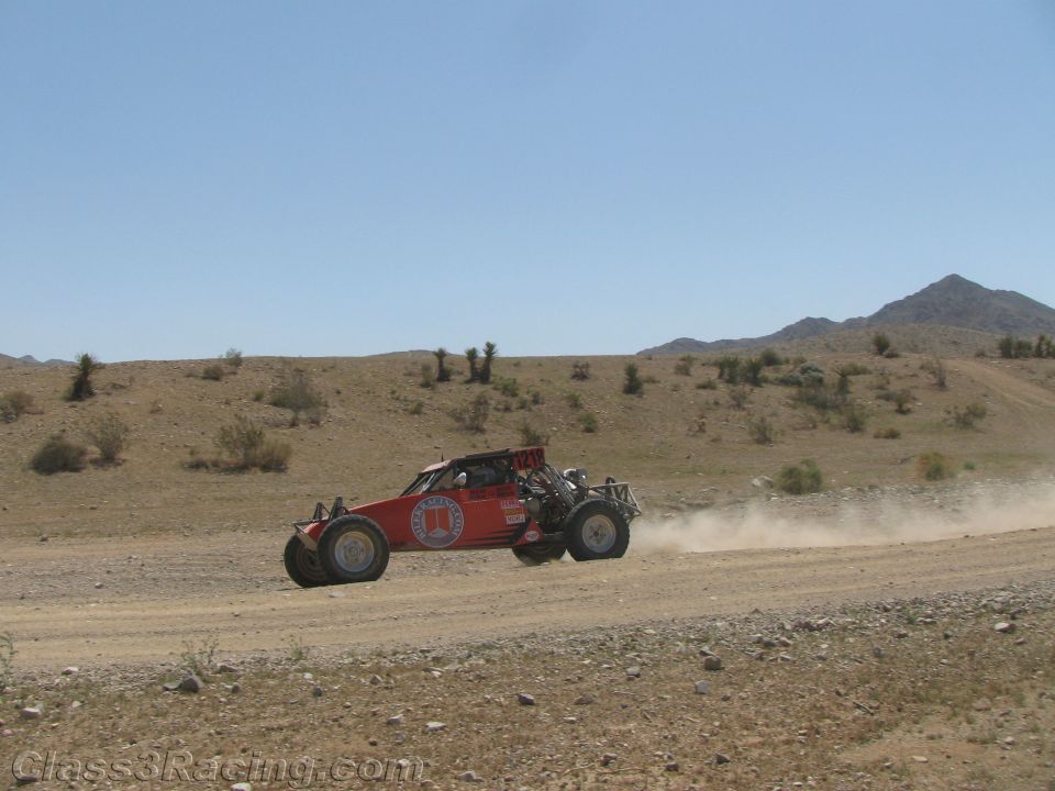 Red single-seat off-road race buggy speeding on a desert road