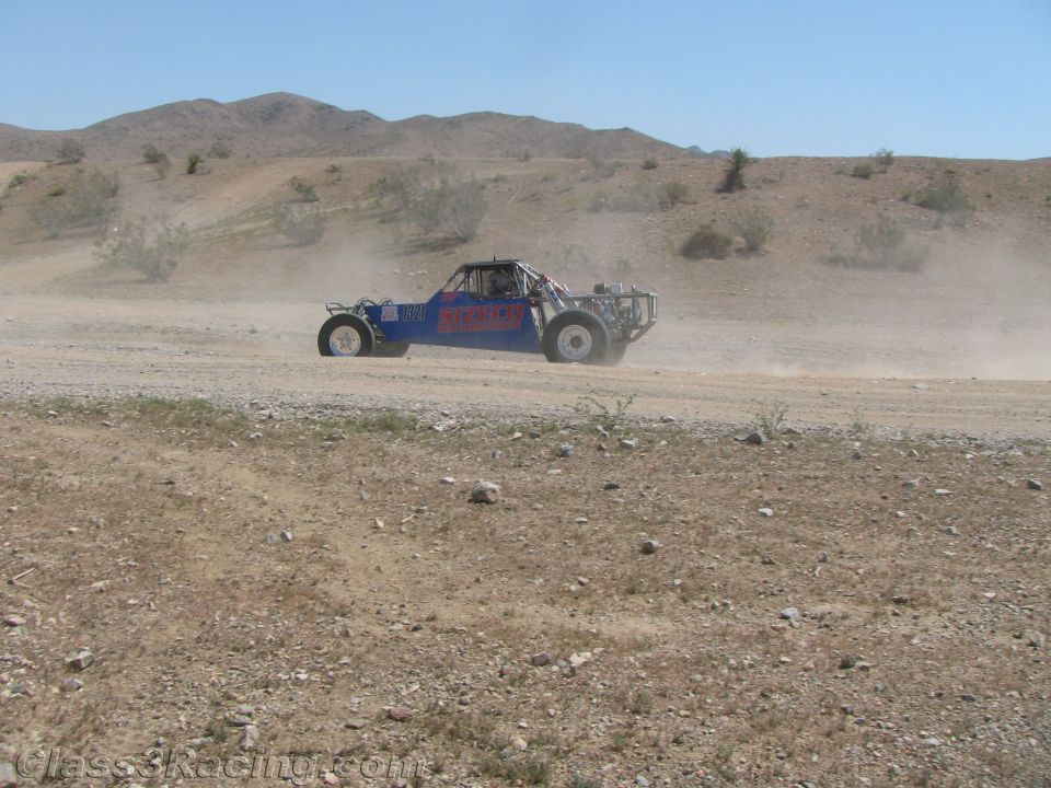 Blue and red off-road race buggy racing across a desert wash