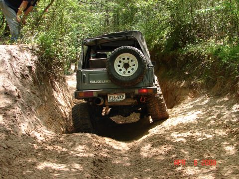 1987 Ford Bronco - Suzuki Samurai tackling a challenging off-road trail with steep inclines and soft dirt.