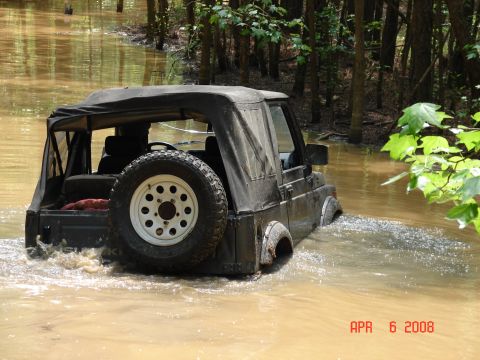1987 Ford Bronco - A Suzuki Samurai navigates through a flooded wooded area, kicking up water as it goes.
