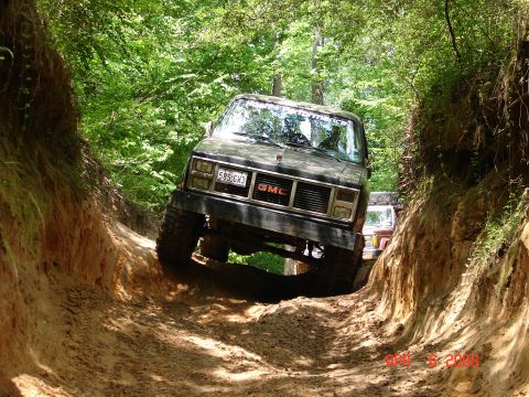 1987 Ford Bronco - A GMC SUV drives through a challenging off-road trail with another vehicle visible behind it.