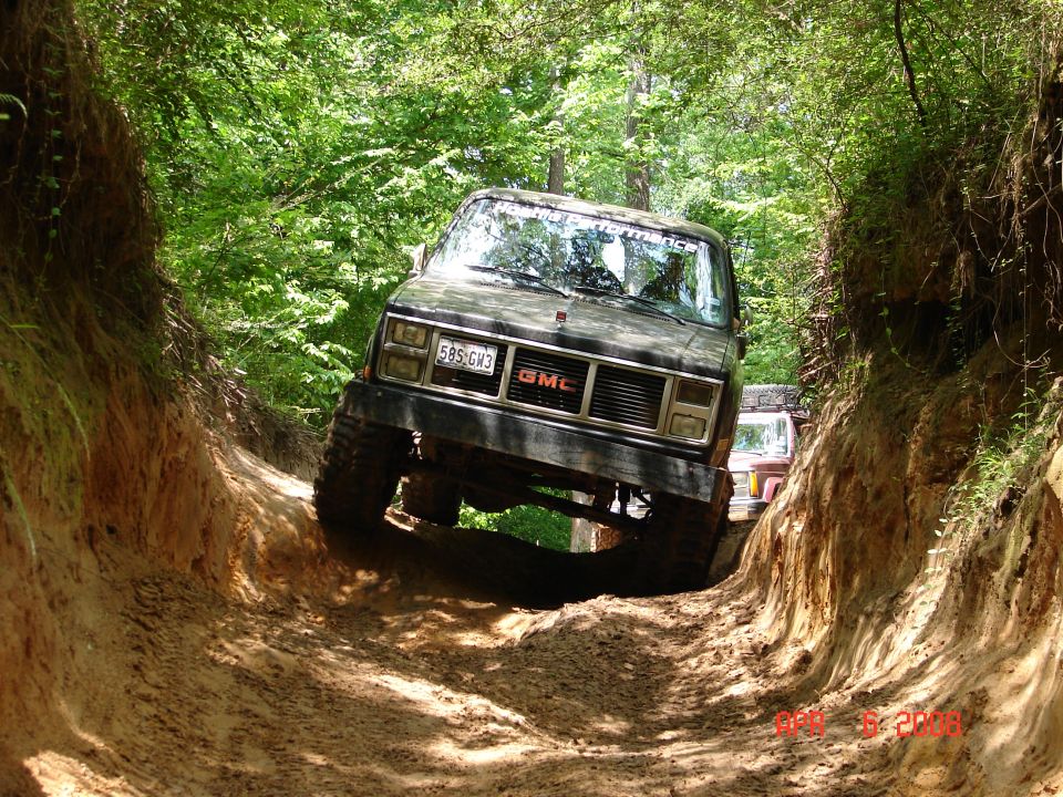 Dark GMC SUV navigating a muddy off-road trail with steep dirt banks