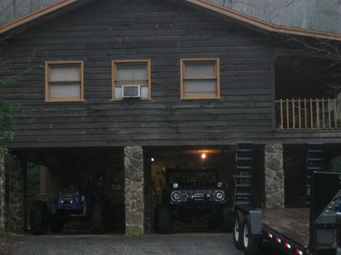 1992 Ford Mustang - Two off-road vehicles are parked under a rustic wooden cabin, with a trailer visible in the foreground.