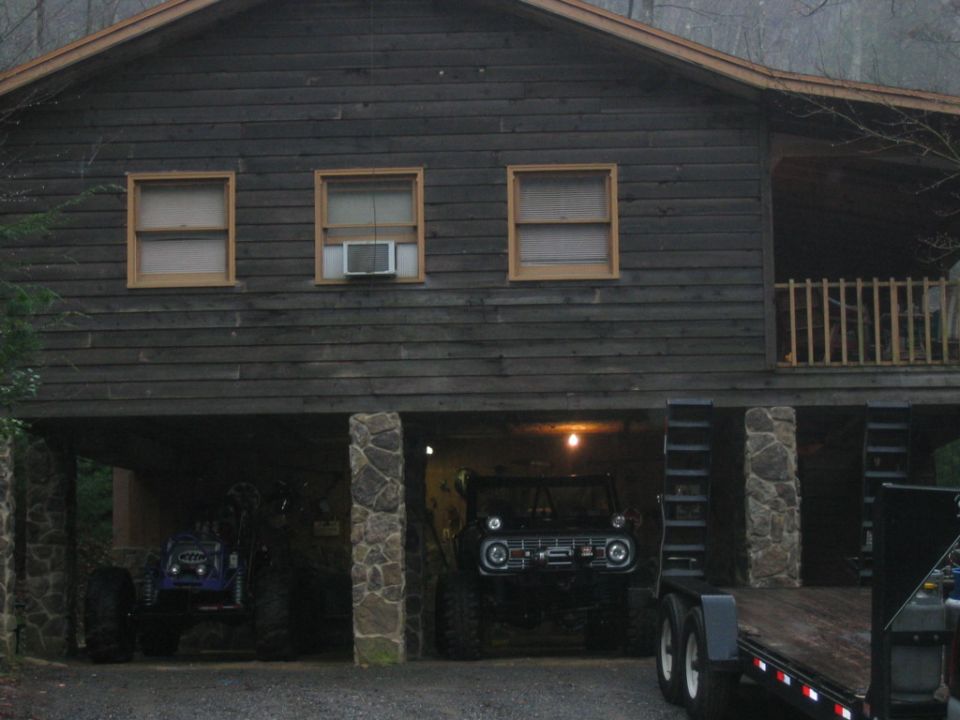 Two off-road vehicles parked under a wooden cabin, one black and one blue