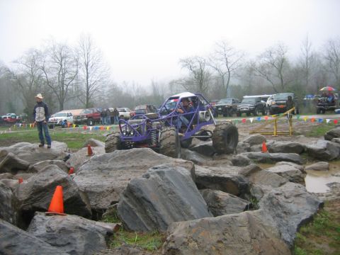 1992 Ford Mustang - Custom buggy tackles a rocky obstacle course with spectators and other vehicles nearby.