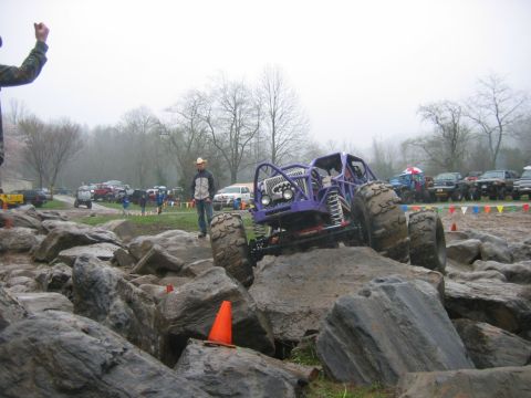 1992 Ford Mustang - A custom-built purple monster truck tackles a challenging rock crawling course on a foggy day.