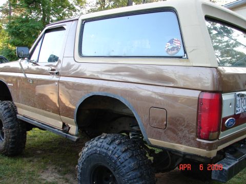 1987 Ford Bronco - A brown 1987 Ford Bronco with lifted suspension and large tires is parked outdoors.