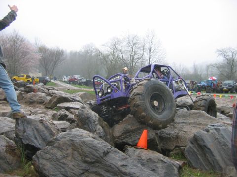 1992 Ford Mustang - A custom-built purple buggy tackles a challenging rock obstacle during an off-road event, with spectators and other vehicles present.