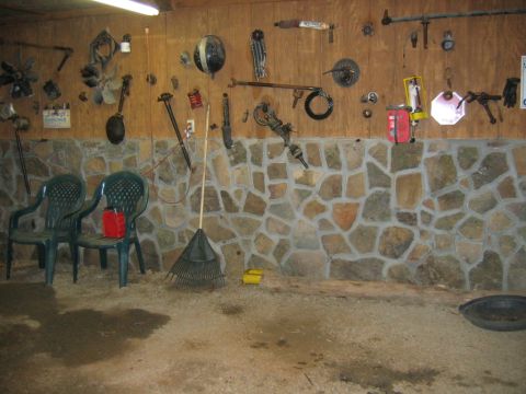 1992 Ford Mustang - A garage interior displays various tools and automotive parts mounted on a wood-paneled wall above a stone foundation.