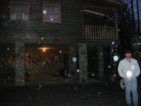 1992 Ford Mustang - A man stands outside a rustic wooden house with stone pillars supporting the upper level.