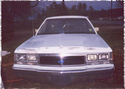 1991 Ford Crown Victoria - Frontal view of a white sedan with a chrome grille and a blue Ford emblem, parked outdoors.