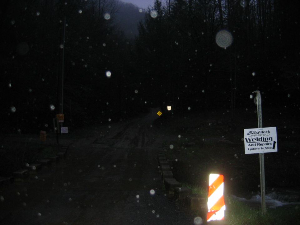 Sign for Steel Rock Offroad Welding and Repairs with a dark, wet road and trees in the background