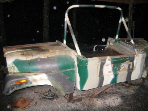 1992 Ford Mustang - The body of a camouflaged Jeep sits on blocks, appearing to be in a state of disrepair.