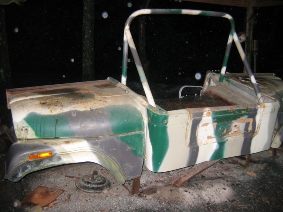 Camouflaged Jeep body, looks like it's missing the engine and wheels