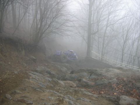 1992 Ford Mustang - A blue off-road buggy is seen on a steep, rocky incline surrounded by fog and trees.